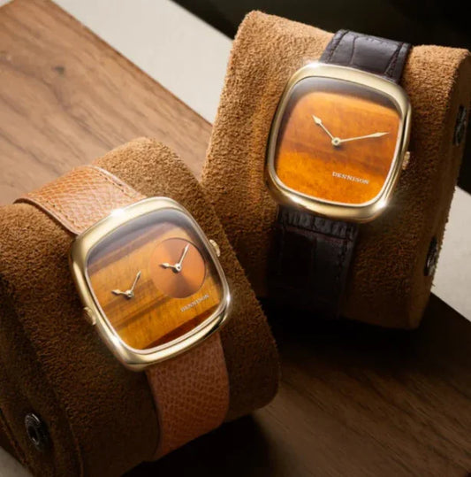 Two luxury square gold wristwatches with brown and black leather straps displayed on suede holders