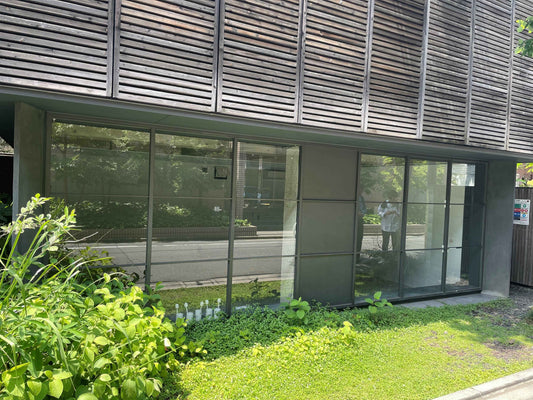 大きなガラス窓と木製外壁が特徴的な店舗外観、緑の植栽が並ぶ