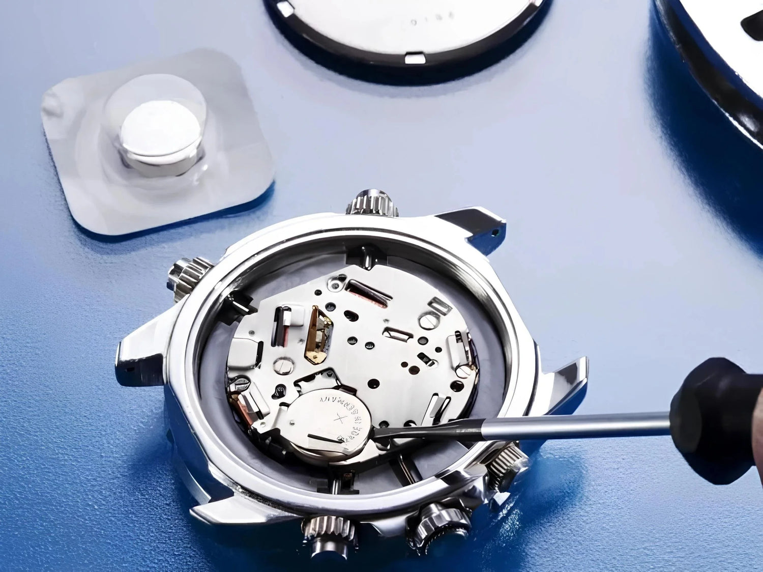Watch back open, technician using screwdriver for battery change and repair on blue surface