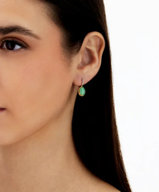 女性がエメラルドグリーンの宝石付きピアスを着用している耳元のアップ